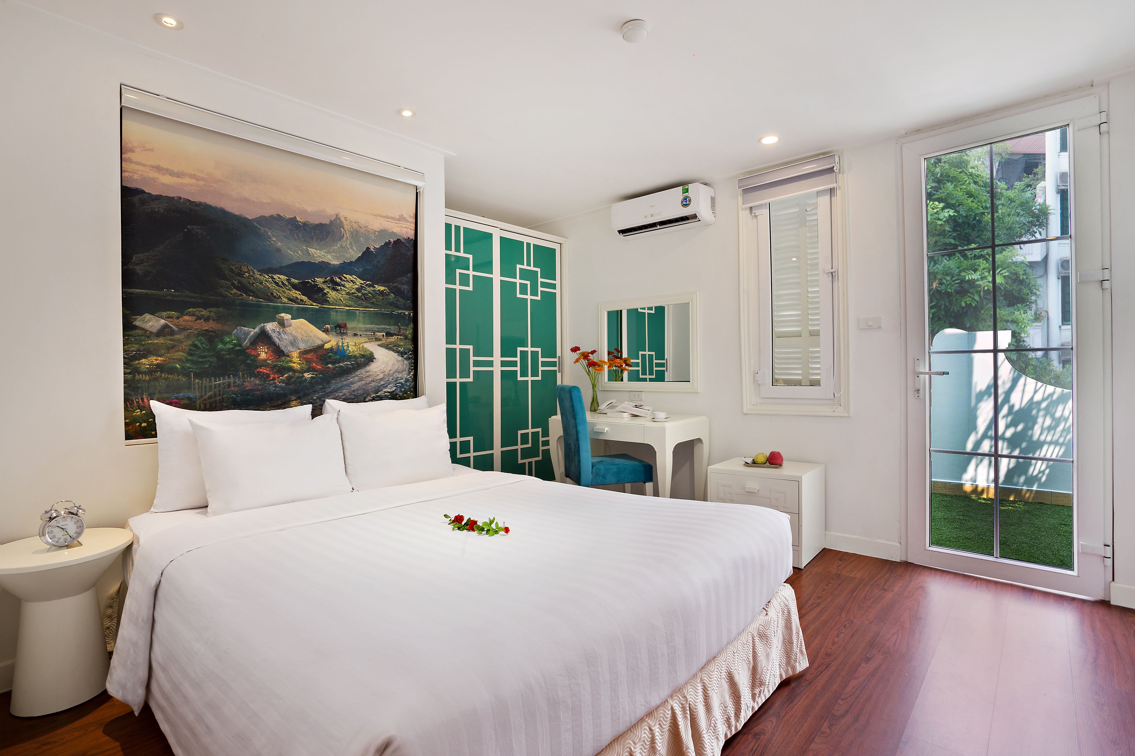 Habitación de hotel con una cama grande, un escritorio, una silla, una mesita, un espejo y vistas al exterior.