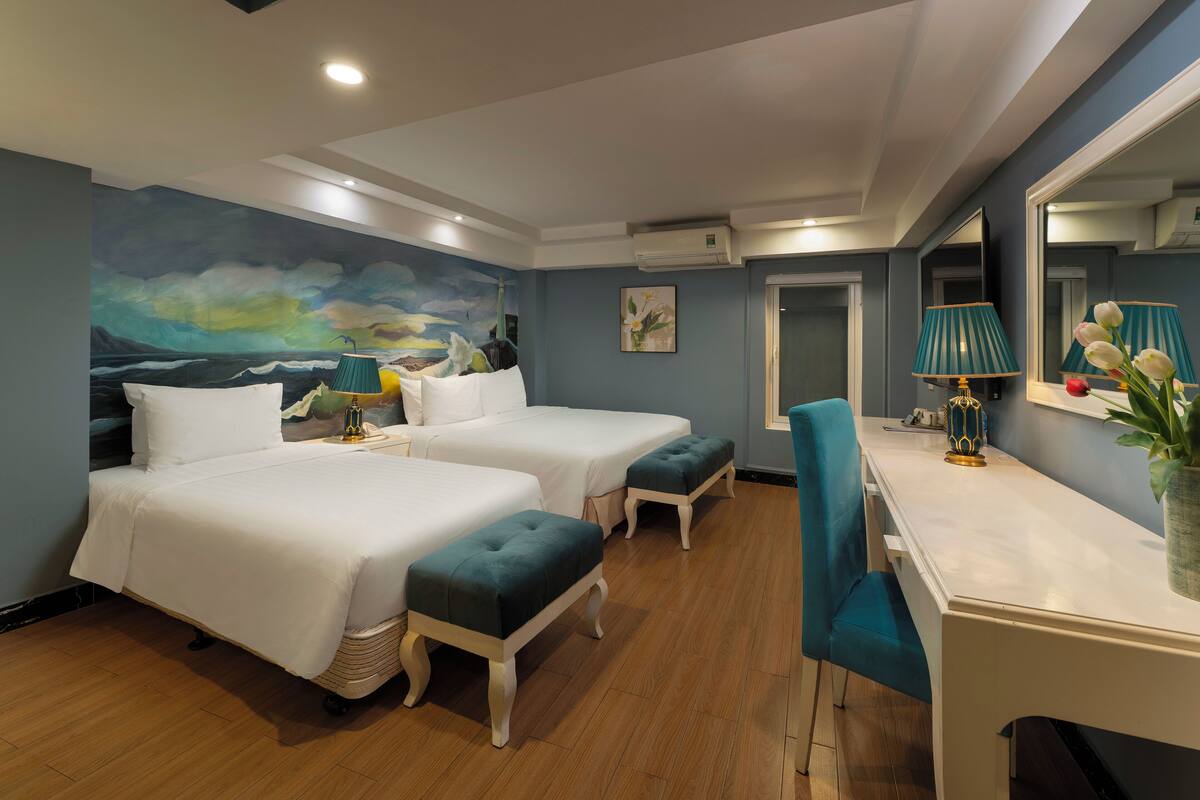A hotel room with two beds, a desk, a chair, a large painting on the wall, and a mirror.