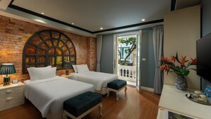 A hotel room with two beds, a brick wall, a large arched window, a balcony with a view, and a TV on a white table.