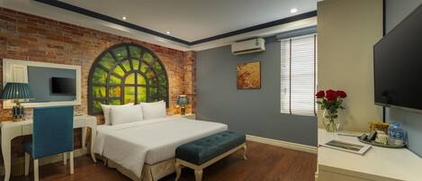 A bedroom with a brick wall, a large window, a bed, a desk, and a TV.