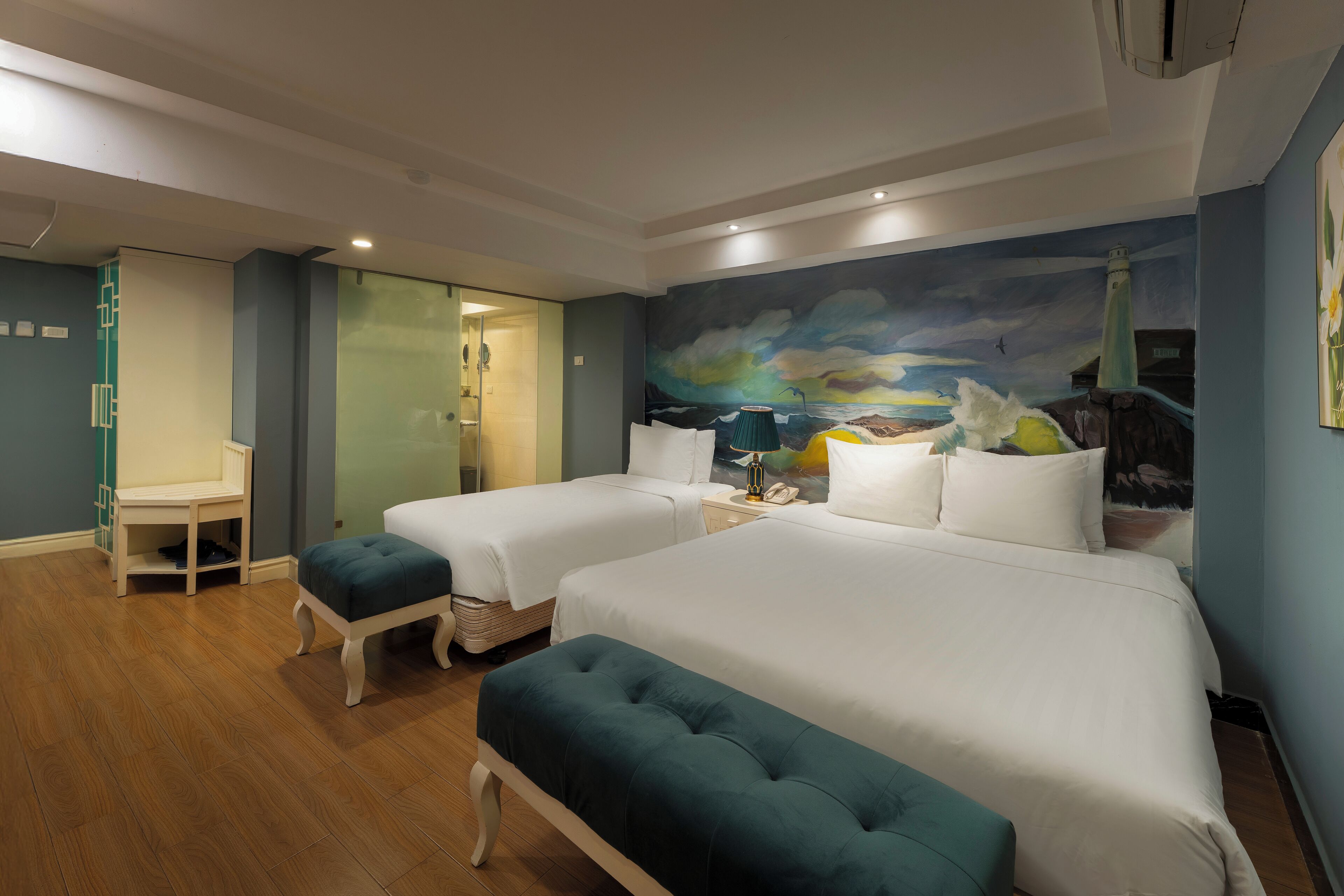 A hotel room with two beds, a desk, and a mural of a seascape.