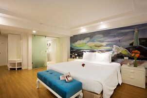 A bedroom with a large bed, a blue bench, a nightstand with a vase of flowers, and a mural of a lighthouse.
