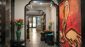 A hallway with a black and white patterned floor, a green vase with orange flowers, and a large abstract painting on the right wall.