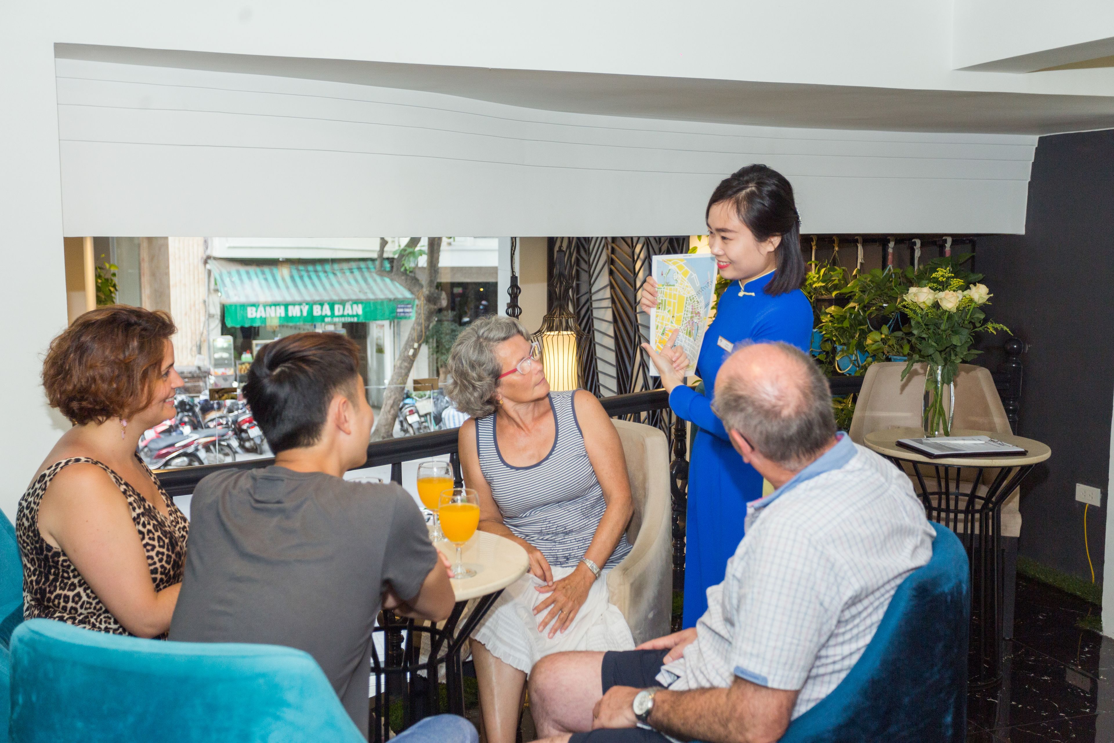 A group of people seated around a table with drinks, in a room with a modern interior design, a green awning outside, and a map on the table.