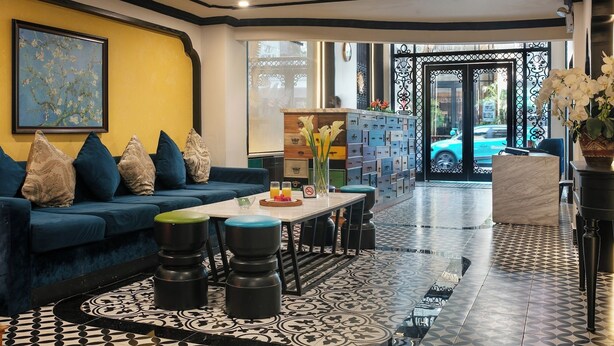 A modern hotel lobby with a blue sofa, black stools, a coffee table, and a patterned floor.