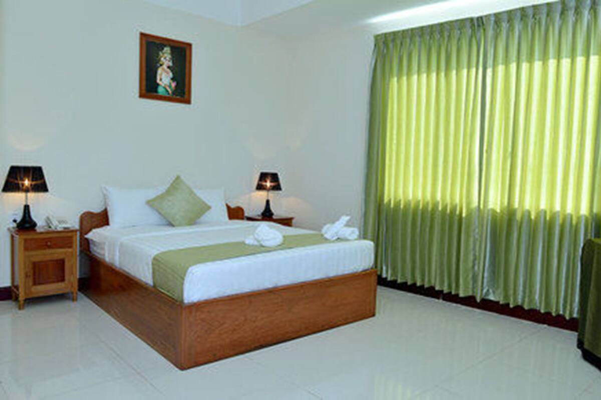 A hotel room with a bed, two bedside tables with lamps, a green curtain, and a painting on the wall.