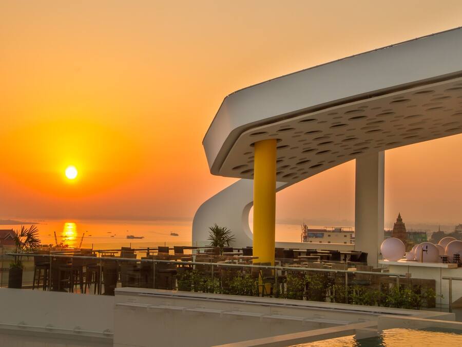 Een terras op het dak met uitzicht op een zonsondergang, een zwembad en moderne architectuur.