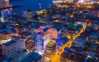 Un hotel de varios pisos con un techo curvo característico, situado en una zona urbana densamente poblada, rodeado de otros edificios.