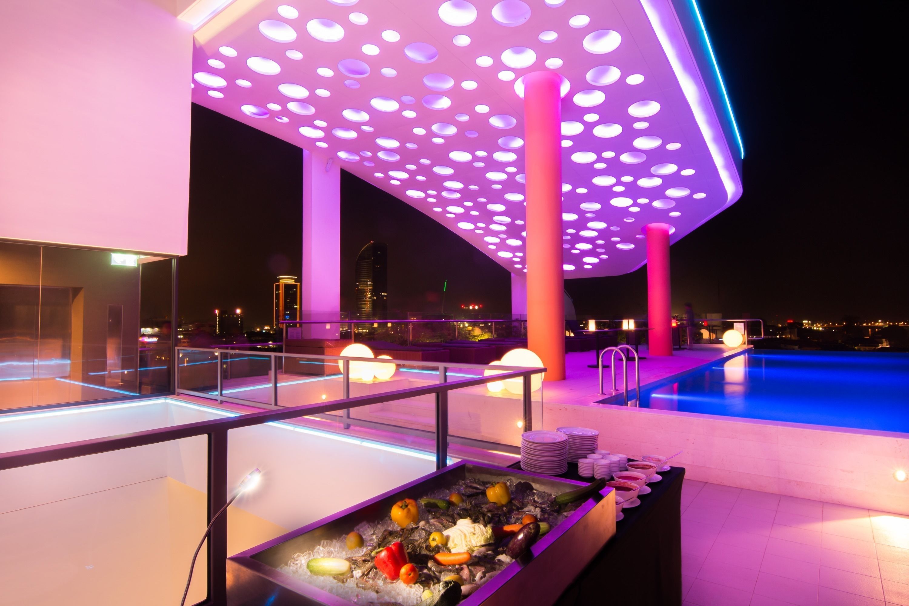 Un espace aménagé au bord de la piscine, avec un buffet, une piscine et un plafond moderne agrémenté de luminaires circulaires.