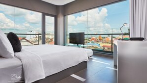 Habitación de hotel moderna con una cama grande, un televisor y un balcón con vistas a la ciudad.