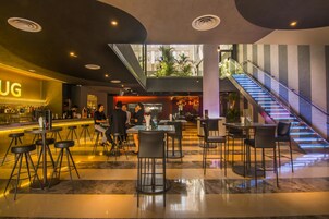 Zona de bar moderna con mostrador, taburetes y una escalera que sube a un nivel superior.