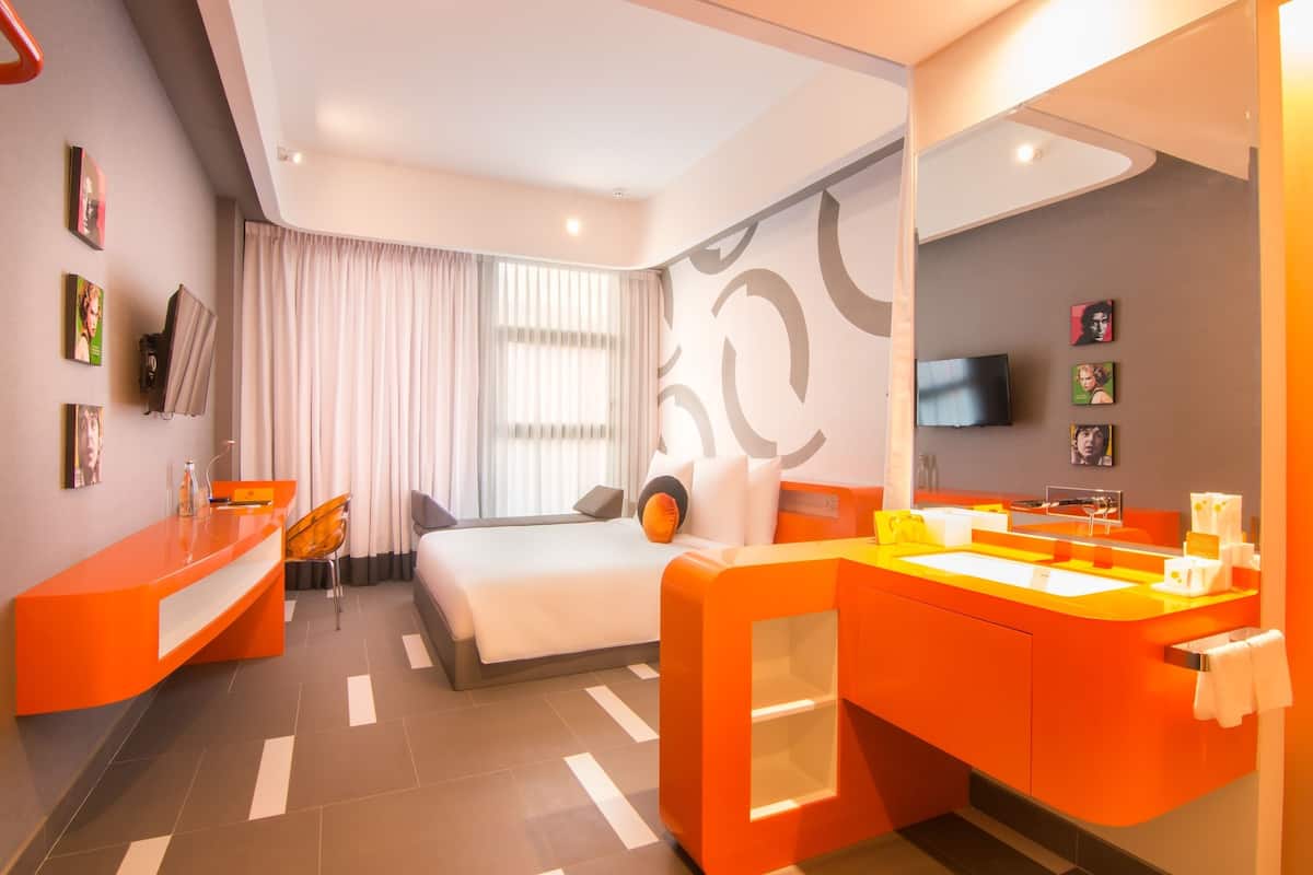 A modern hotel room with a bed, a desk, a bathroom with a mirror, and a TV on the wall.