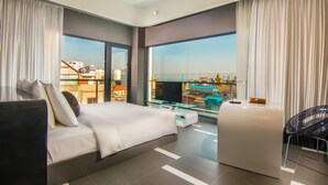 Una habitación de hotel moderna con una cama grande, una zona de estar y un balcón con vistas a la ciudad.