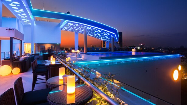 Un bar en la azotea con piscina, mesas al aire libre e iluminación ambiental.