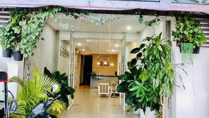 Une entrée bien éclairée, agrémentée de plantes suspendues, un comptoir d’accueil et un espace repas visible au fond.