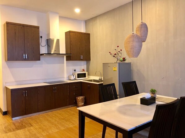 Une cuisine moderne avec des meubles de couleur bois foncé, un plan de travail blanc et un coin repas comprenant une table et des chaises.