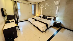 Une chambre d’hôtel avec deux lits, un bureau, une télévision et un mur décoré d’une fresque représentant un arbre.