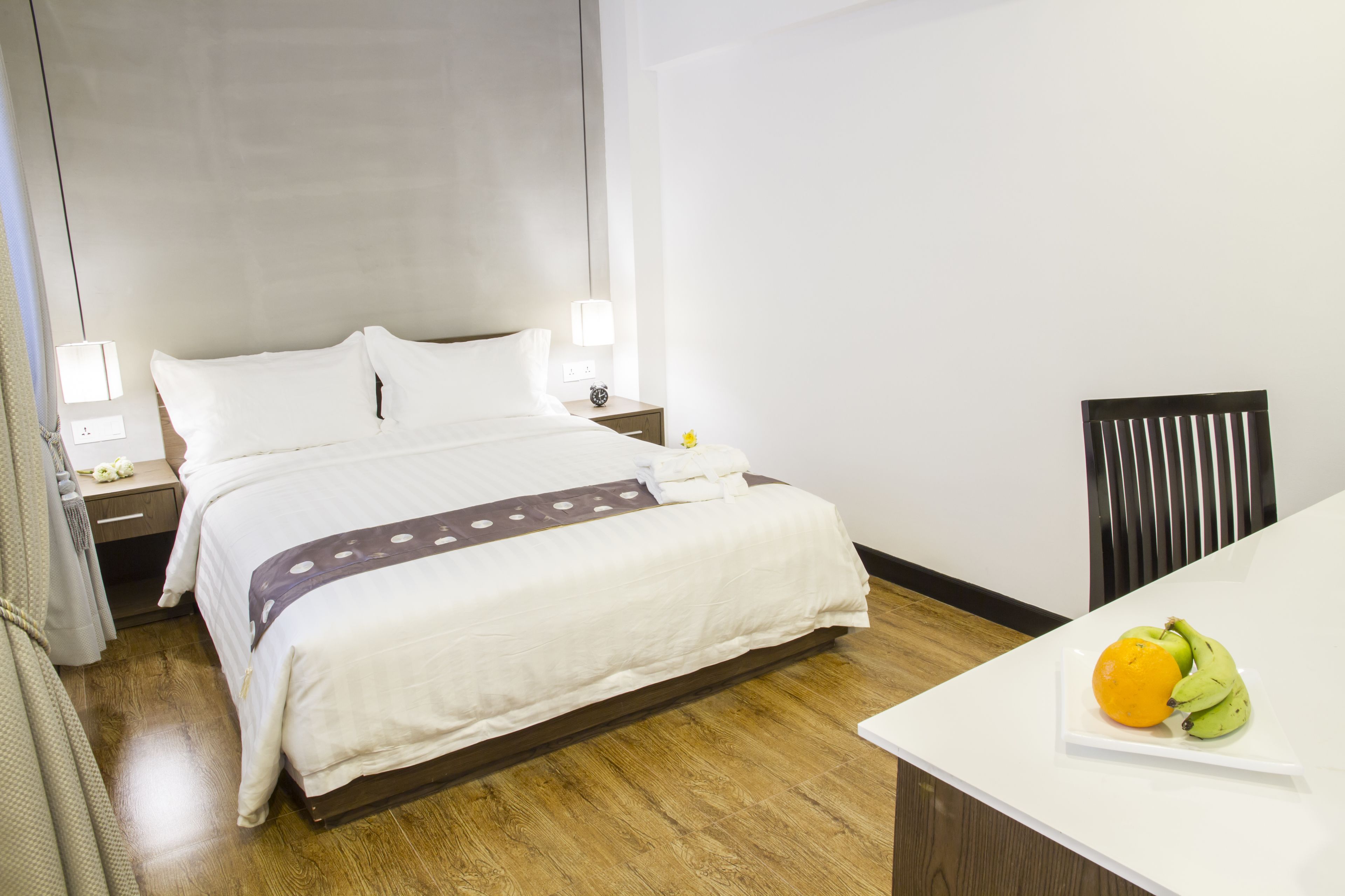 Quarto de hotel com cama grande, mesas de cabeceira, escrivaninha e uma cadeira.