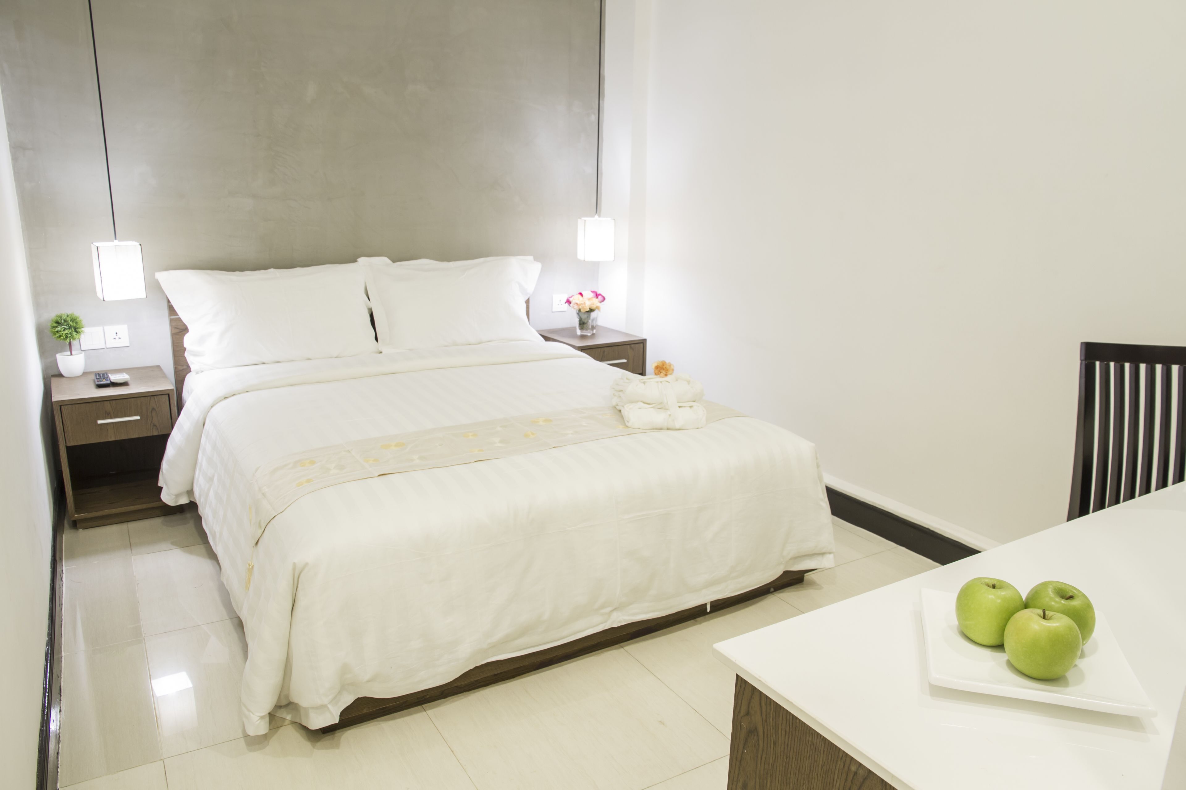 A neatly made bed with white linens, a bedside table with a lamp, and a small vase with flowers.