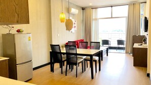 Une cuisine moderne équipée d’un réfrigérateur, d’une table à manger et de chaises. Une fenêtre avec des rideaux offre une vue sur l’extérieur.