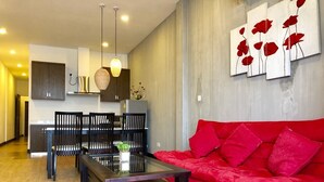 Un salon moderne avec un canapé rouge, une table basse en verre et un coin repas comprenant une table et des chaises en bois.
