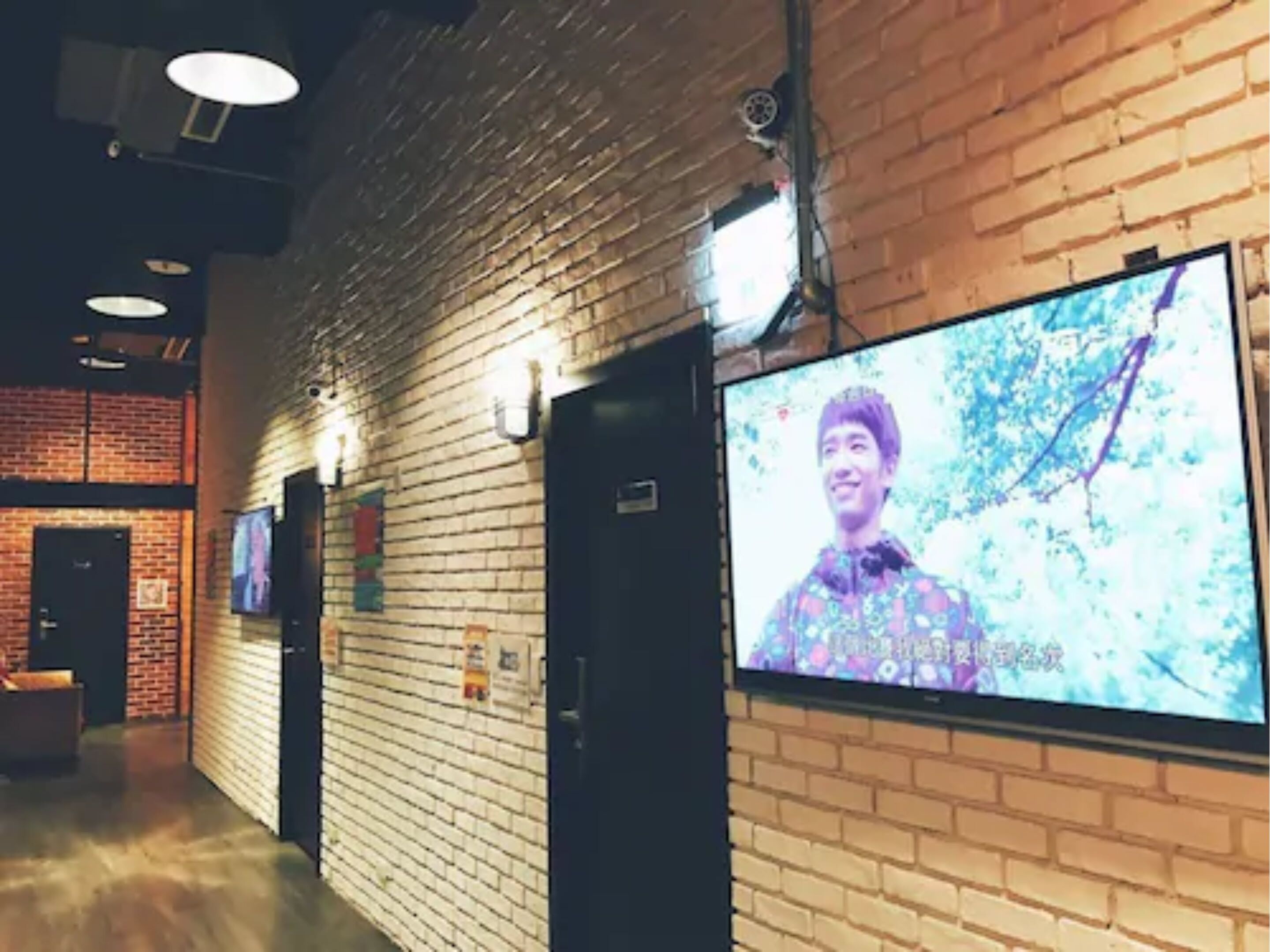 A hallway with brick walls, a large screen displaying a person, and a door with a sign.