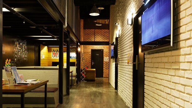 A corridor with a brick wall, a wooden bench, a table with papers, and a television mounted on the wall. - Angels' Hostel - Taipei Ximen (Taipei)