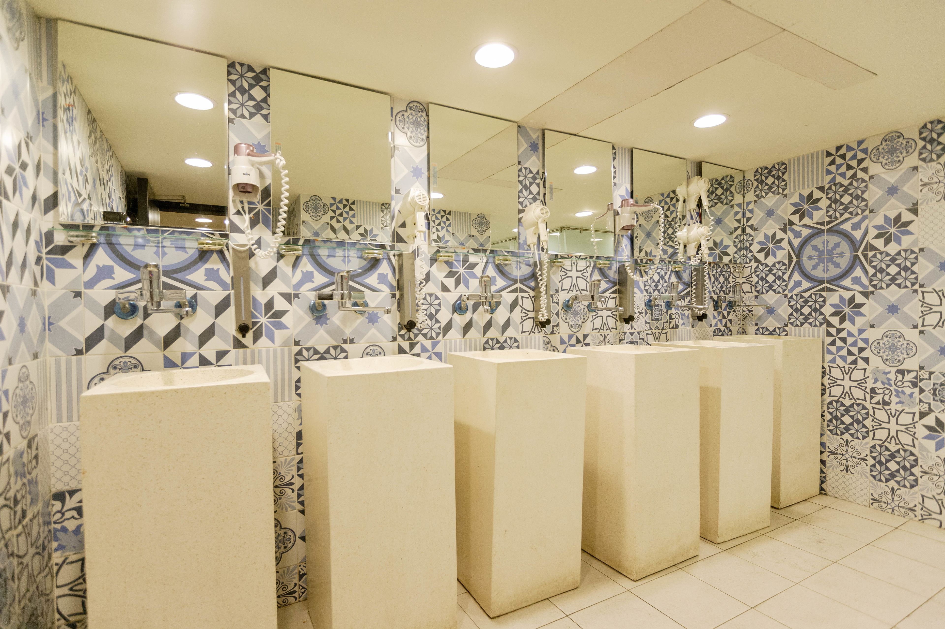 Des toilettes publiques dotées de plusieurs lavabos et de miroirs, de murs carrelés ornés de motifs géométriques et d’un sol carrelé.