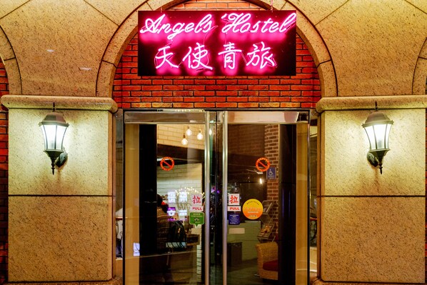 A hotel entrance with a neon sign, glass doors, and two wall-mounted lights. - Angels' Hostel - Taipei Ximen (Taipei)