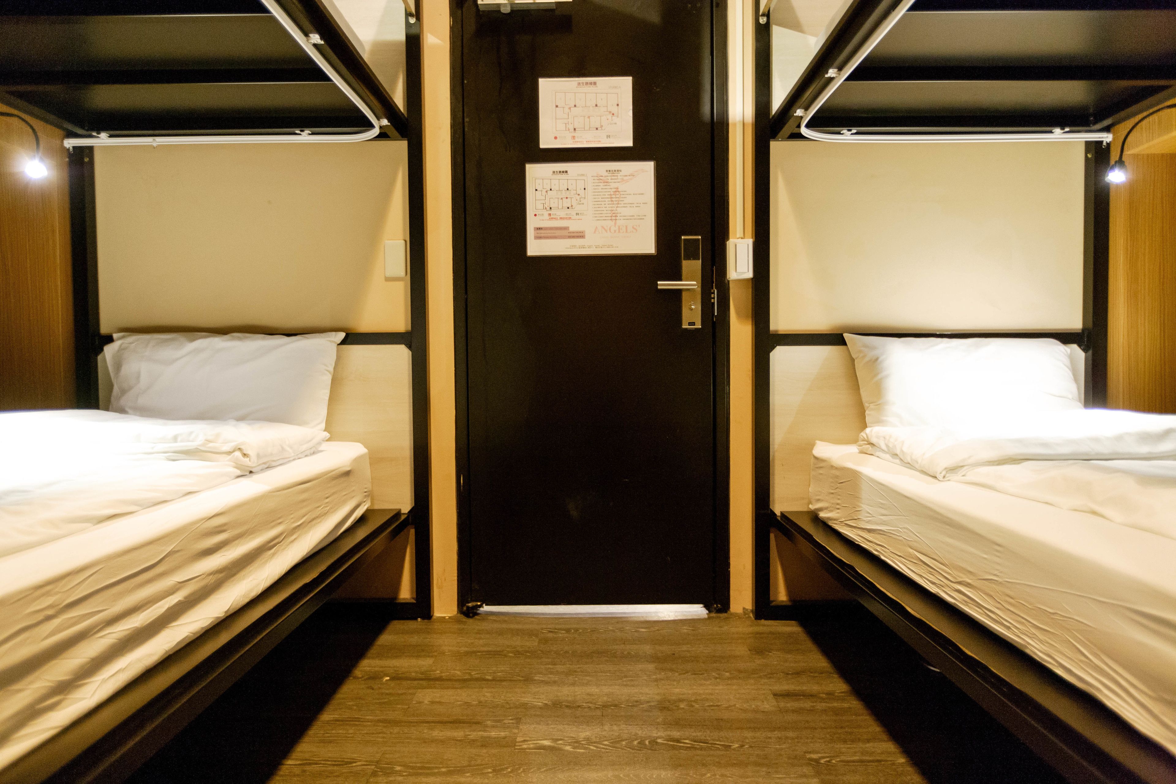 A narrow corridor with two beds on either side, a door at the end, and a small sign on the wall.
