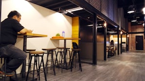 A modern interior with a person sitting at a wooden table, multiple bar stools, and a brick wall. - Angels' Hostel - Taipei Ximen (Taipei)