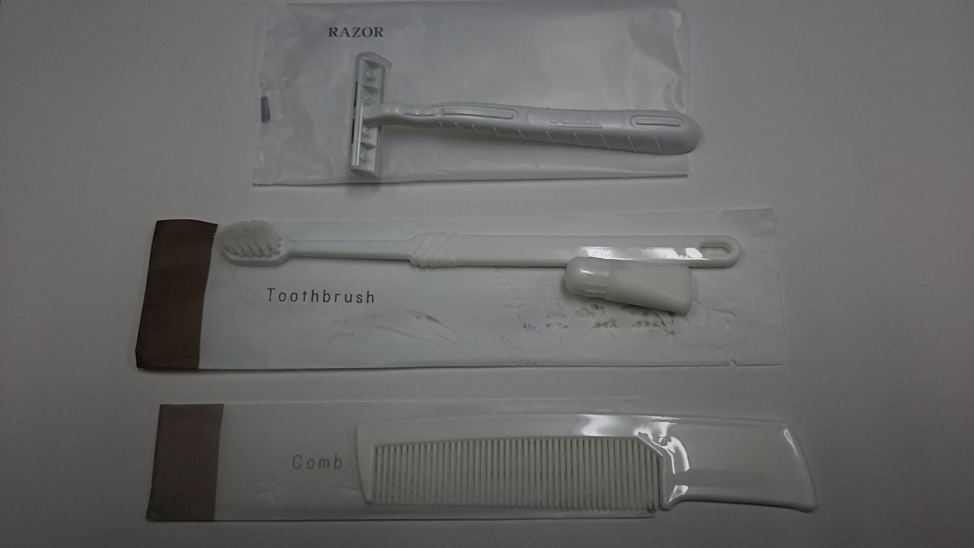 Trois accessoires de toilettage : un rasoir, une brosse à dents et un peigne, chacun dans son propre emballage.