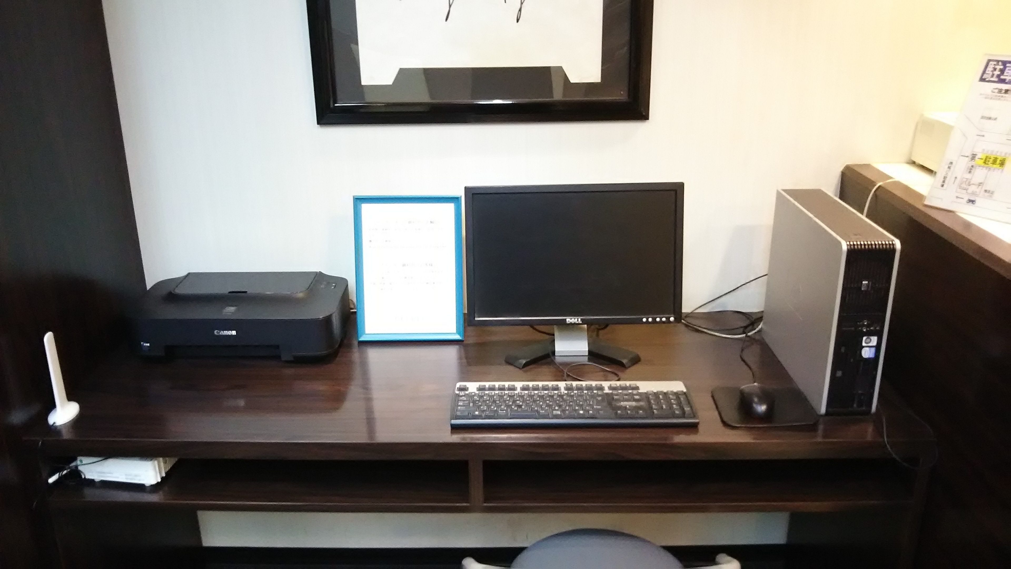 Ein Holztisch mit einem Desktop-Computer, einem Drucker und einem gerahmten Dokument.