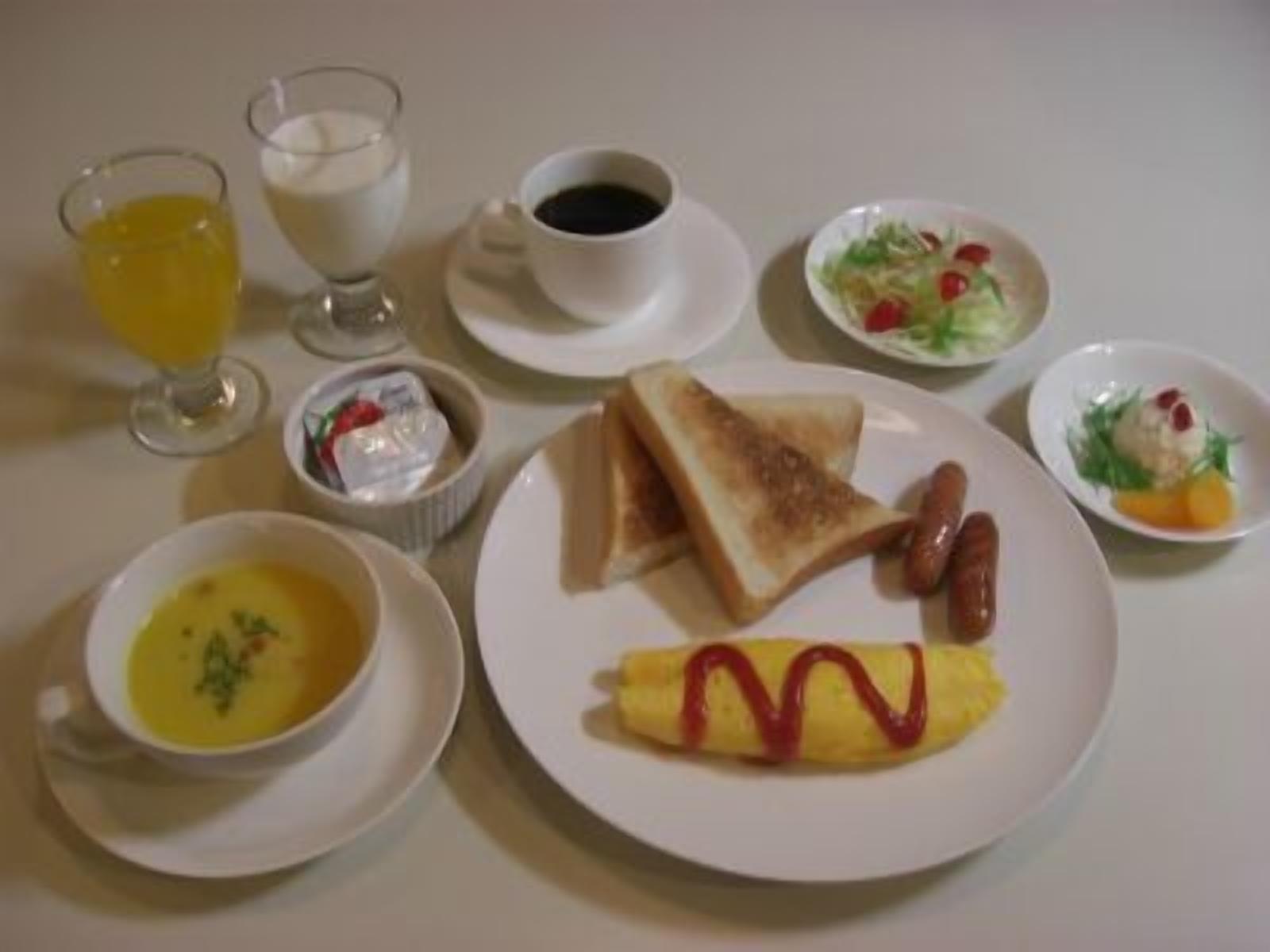 A breakfast setting with toast, sausage, an omelette, soup, and various side dishes.