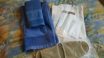 A bed with a colorful bedspread, a folded blue towel, a white pillow, and a beige mesh bag.