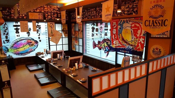 A restaurant interior with a long counter, cushions, and various decorations including posters and banners. - Palude Kushiro (Kushiro)