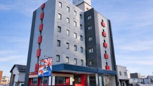 A multi-story hotel with a modern design, featuring a prominent red and grey facade, a visible entrance with a red awning, and a signboard with Japanese text. - Palude Kushiro (Kushiro)