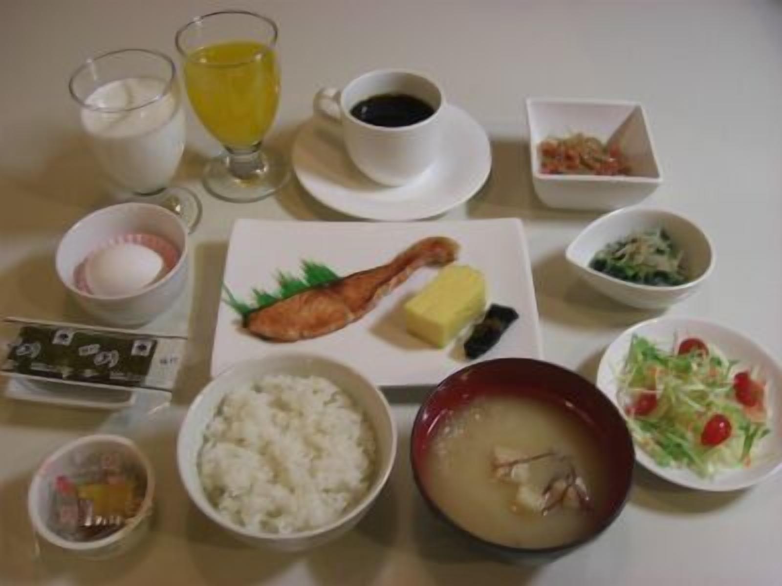 Una mesa servida con diversos platos, entre ellos arroz, sopa y un guiso de pescado, además de bebidas y aderezos.