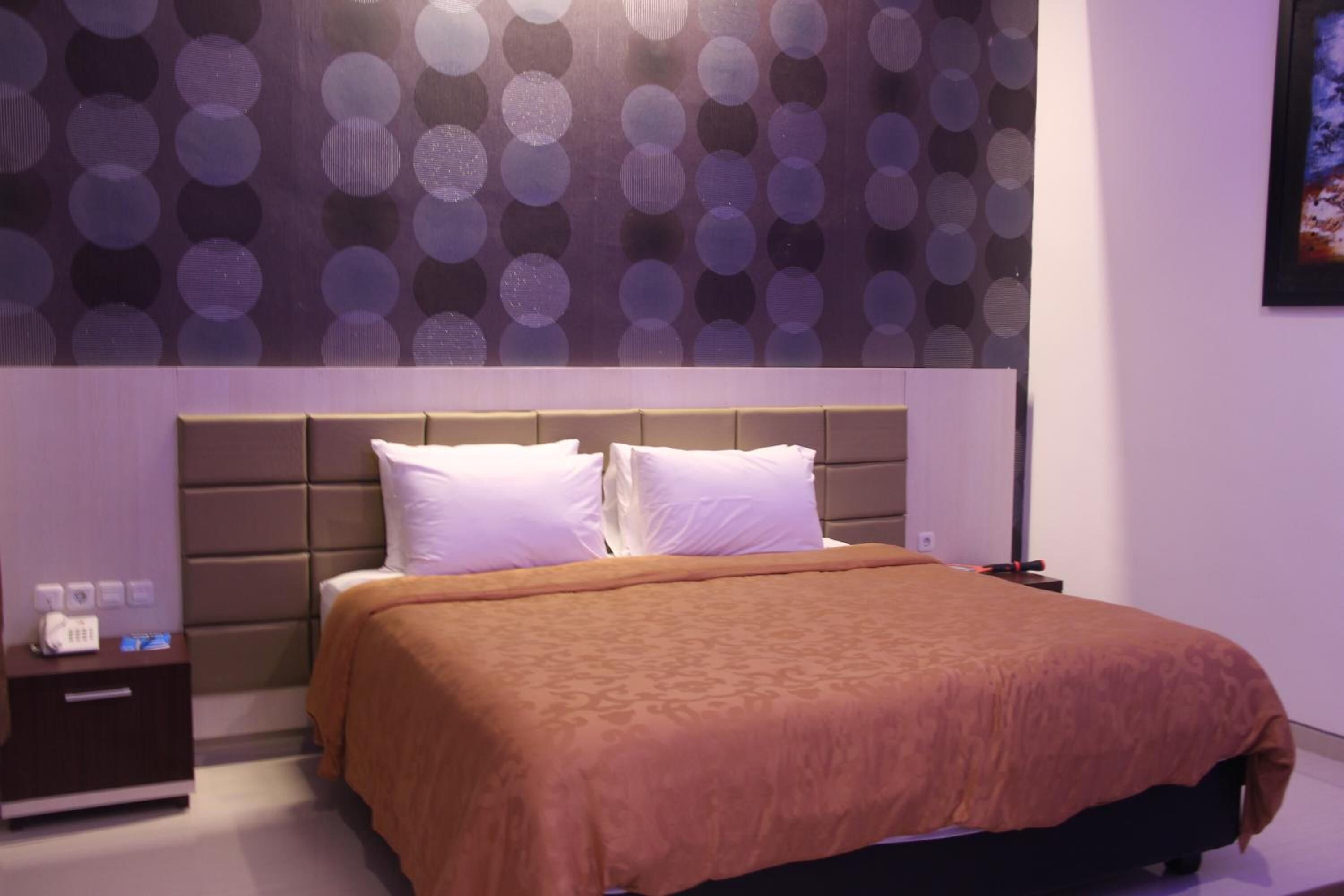 Ein modernes Hotelzimmer mit einem großen Bett, einem Kopfteil mit kreisförmigem Muster, einem Nachttisch und einem Wandbild.