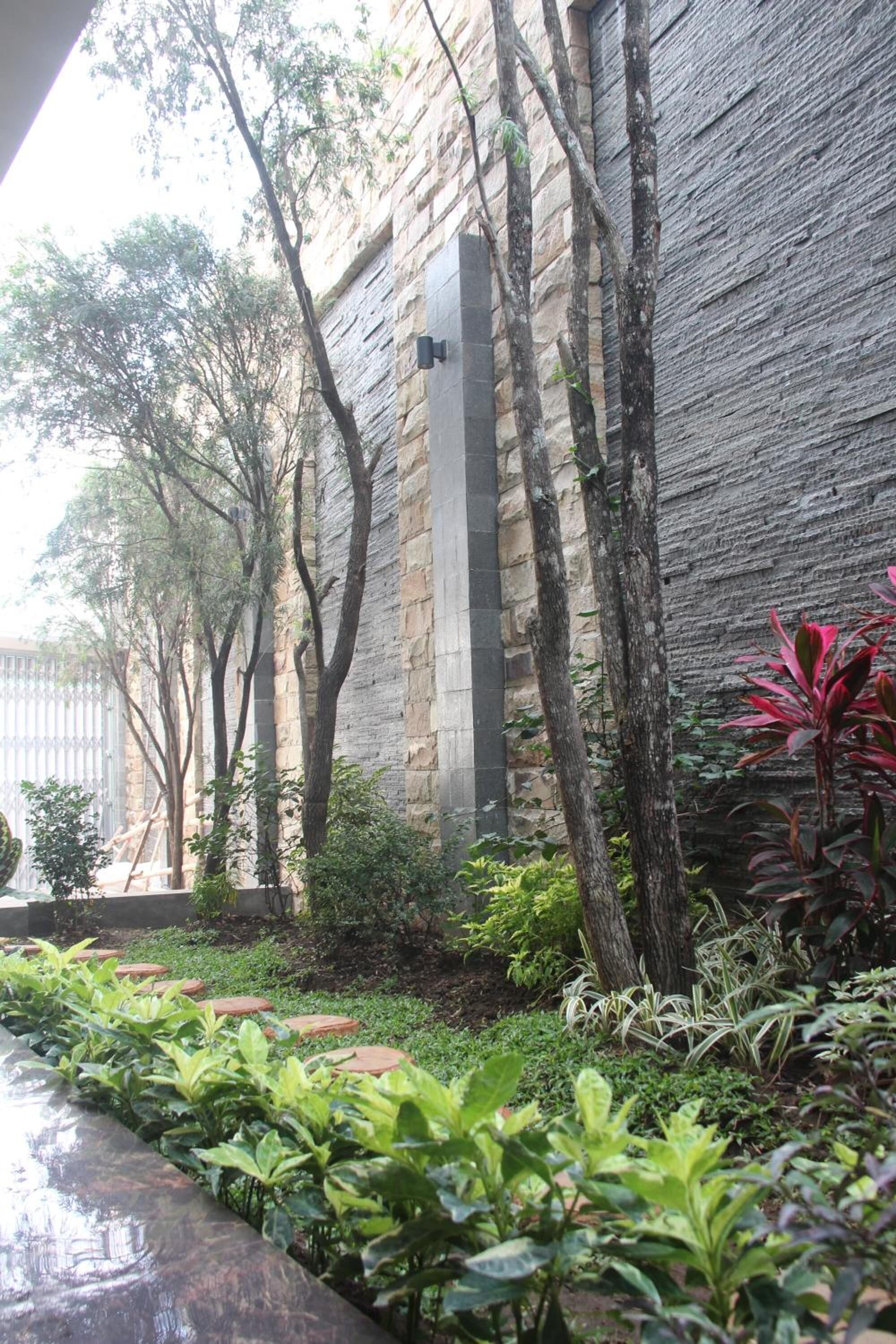 A stone wall with a vertical black structure, surrounded by greenery and trees.