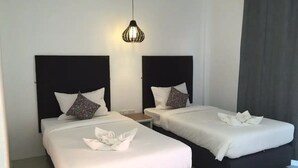A hotel room with two beds, each with a black headboard and white bedding. There is a small bedside table between the beds, and a single hanging light fixture above. - Non Du Lay Guesthouse (Ko Lanta)