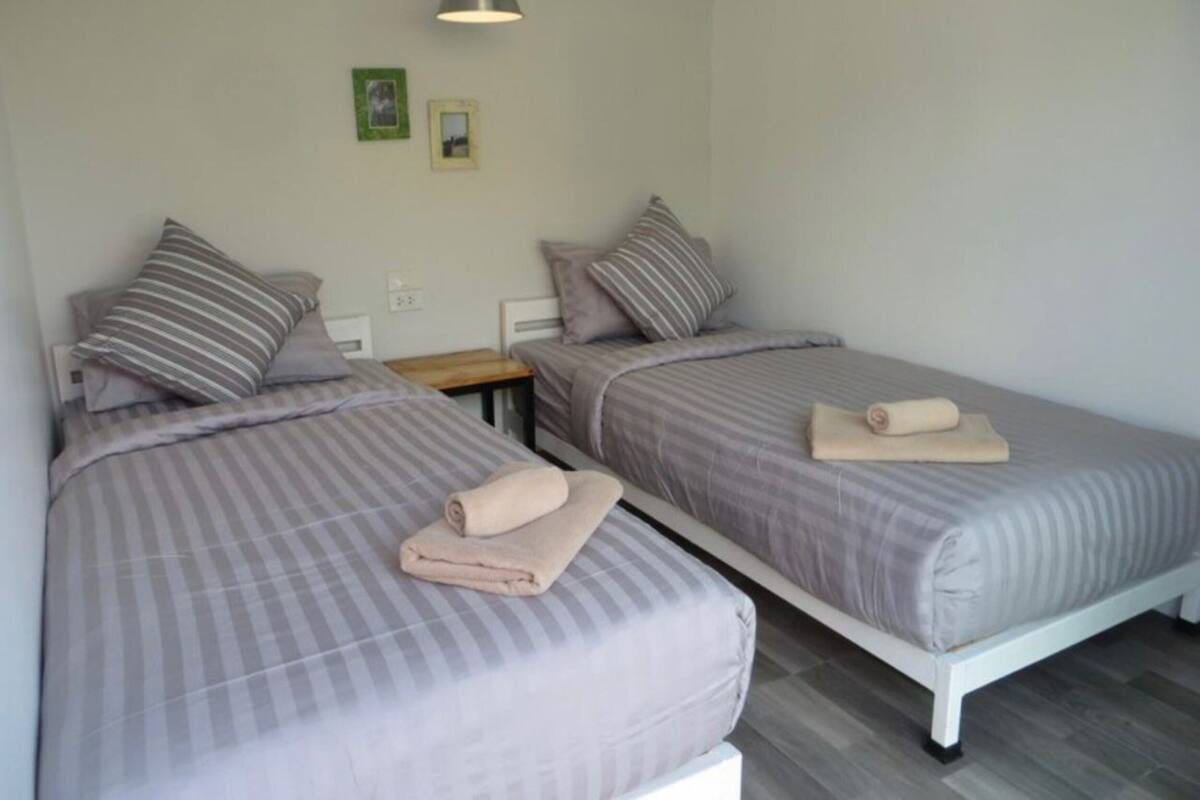 Two single beds with striped bedding and pillows, a bedside table, and a wall-mounted lamp.