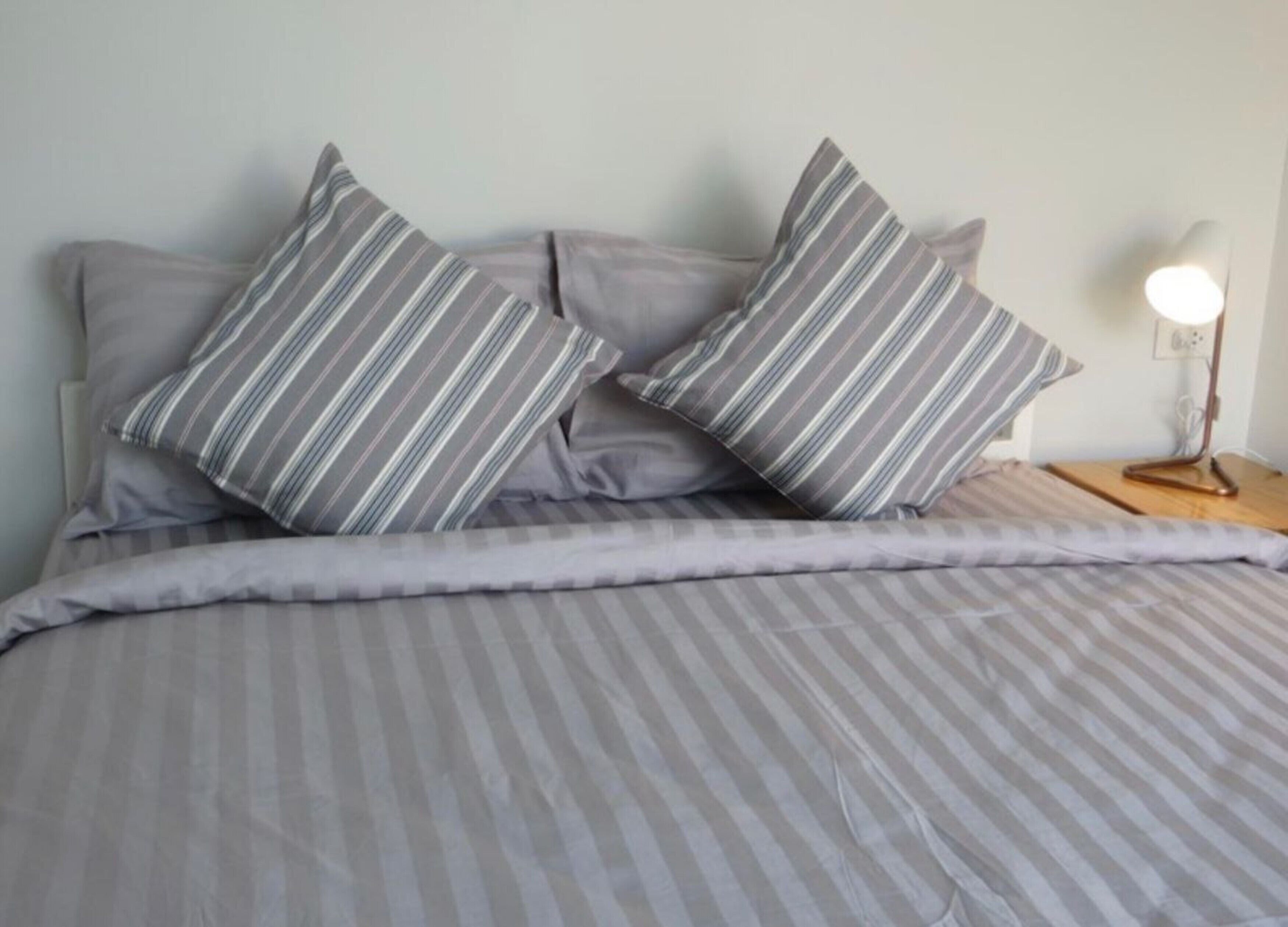 A bed with striped bedding and two pillows, a bedside lamp, and a plain wall.