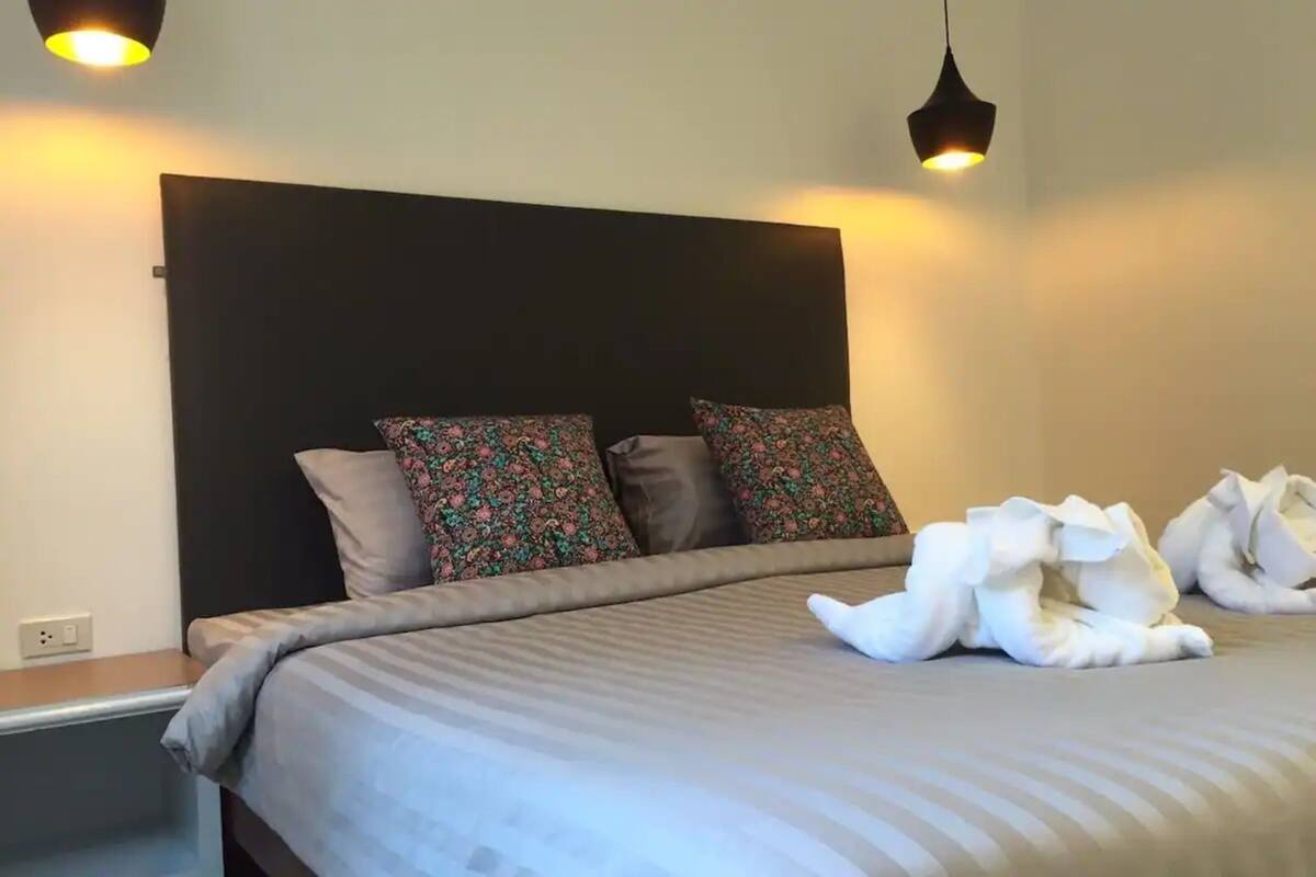 A neatly made bed with floral pillows, a dark headboard, and two pendant lights.