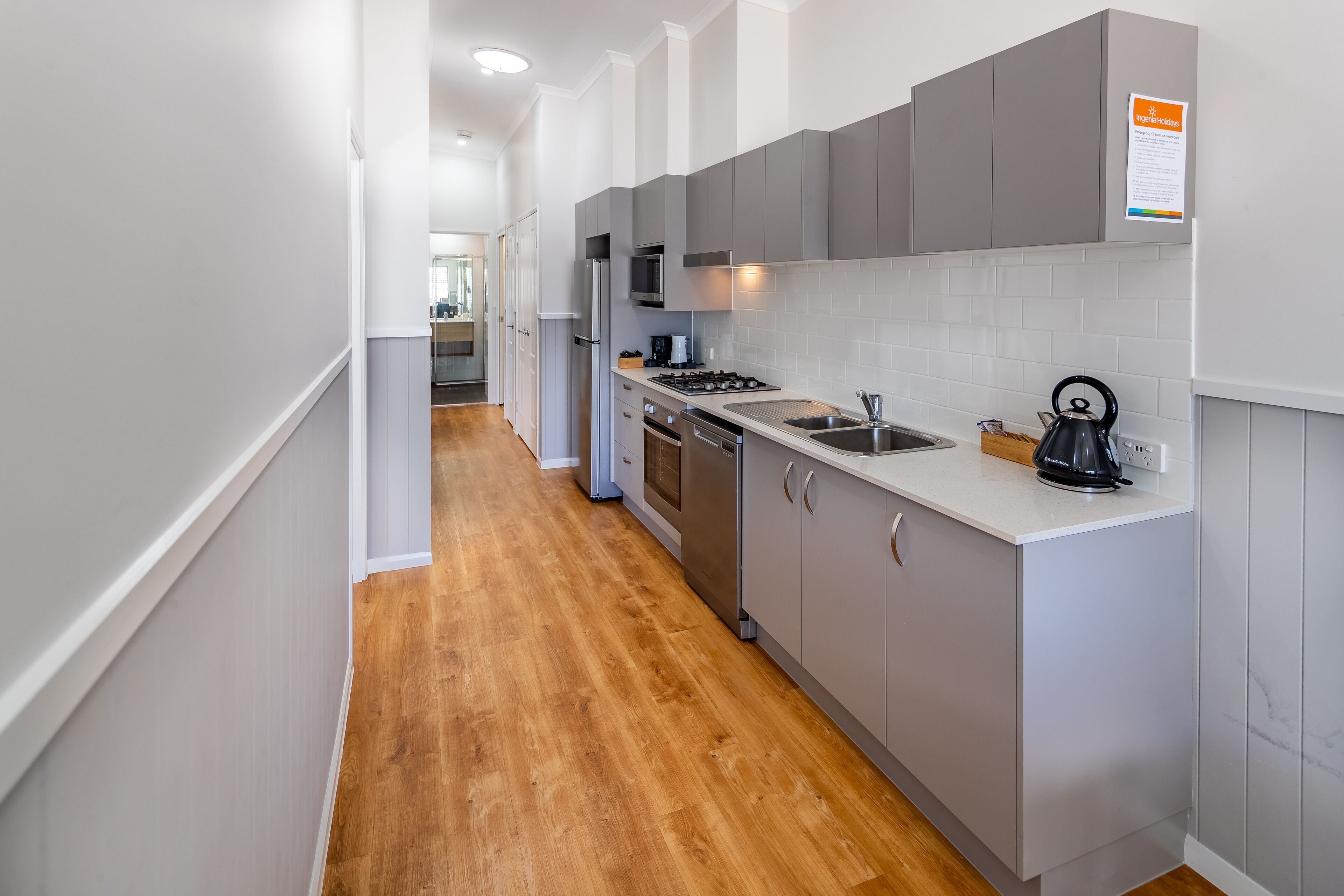 A modern kitchen with grey cabinets, a stainless steel refrigerator, a microwave, and a kettle on the counter.