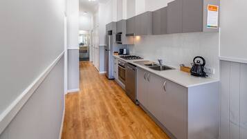 A modern kitchen with grey cabinets, a stainless steel refrigerator, a microwave, and a kettle on the counter.