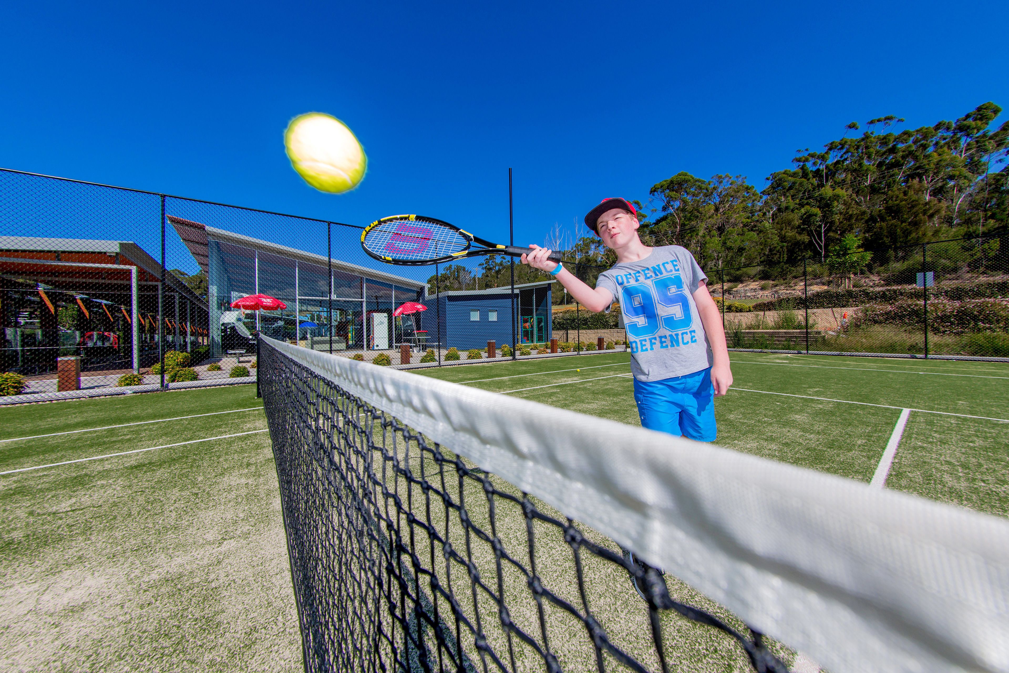 A tennis court with a net, a tennis racket, and a tennis ball in motion.