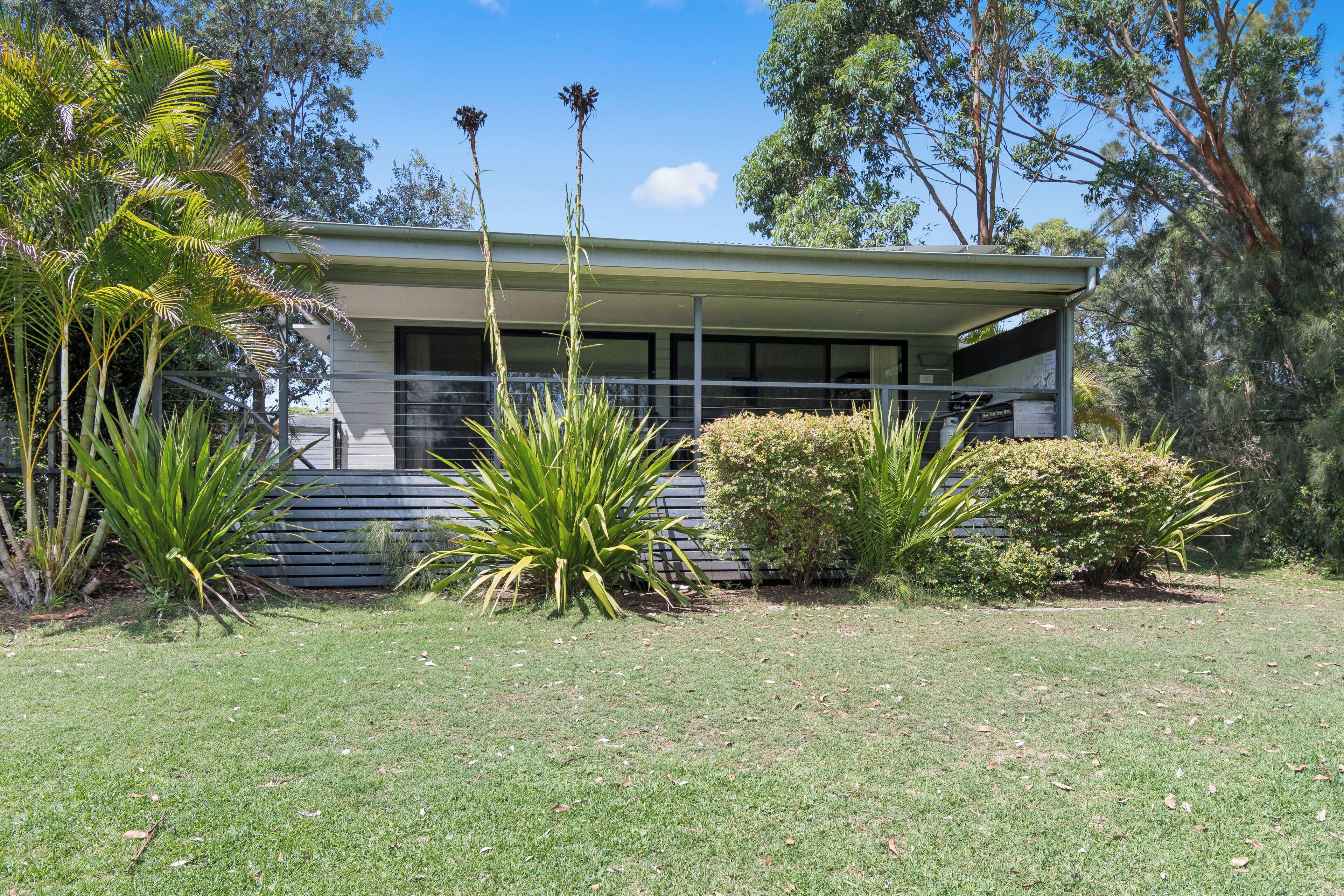 A single-story building with a flat roof, surrounded by a well-maintained lawn and various tropical plants.