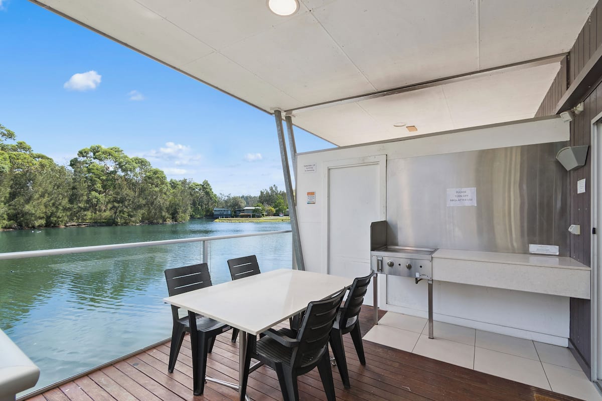 Un espace extérieur abrité, équipé d’une table et de chaises, d’un barbecue et offrant une vue sur un lac.