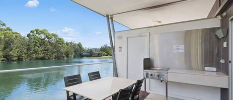 Un espacio exterior cubierto con mesa y sillas, una parrilla y vistas a un lago.